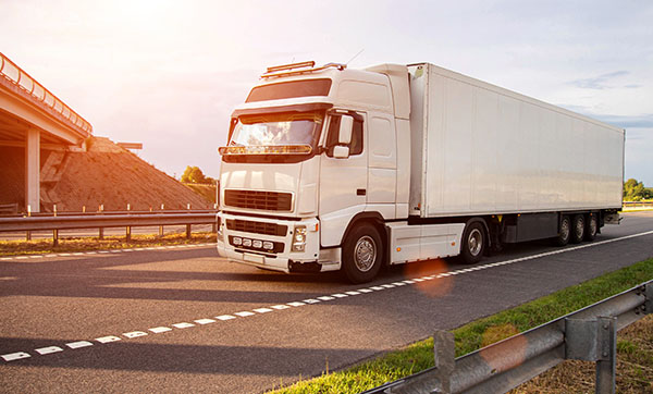 large white truck driving on highway with sunset backdrop and road signs featuring transport and logistics elements related to 18 wheeler