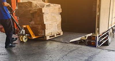 worker using a pallet jack to load boxes onto a delivery truck in a loading dock area transporting goods for distribution