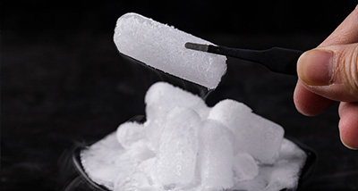 hand holding a tweezers lifting a piece of ice from a mound of ice cubes showcasing the ice's frosty texture and cold appearance ideal for drinks and recipes for six