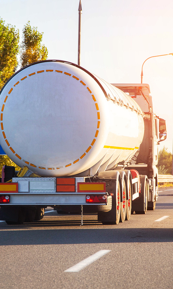 rear view of a large tanker truck with a circular tank on the back driving on a sunny road showcasing smooth transportation of goods and essential services for a streamlined economy