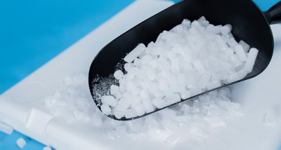 close up of coarse salt in a black scoop on a white cutting board with a blue background ideal for culinary 4 uses and seasoning