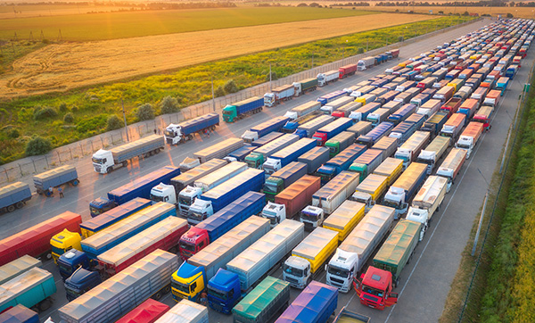an aerial view of a large number of trucks arranged in rows on a wide road with fields in the background showcasing logistics and transportation efficiency
