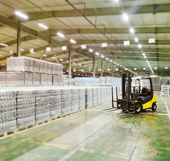 forklift in large warehouse with stacked pallets of 3 crates and other goods